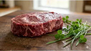 Raw 100% grass-fed beef steak next to fresh forage highlighting pure diet standards.